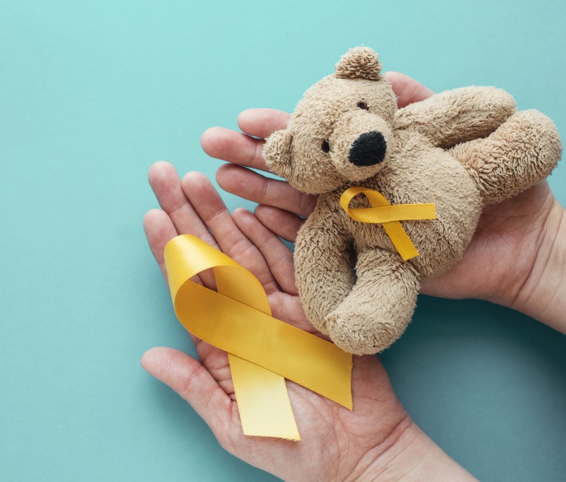 Hands holding children soft toy brown bear with yellow gold ribbon, Childhood cancer awareness
