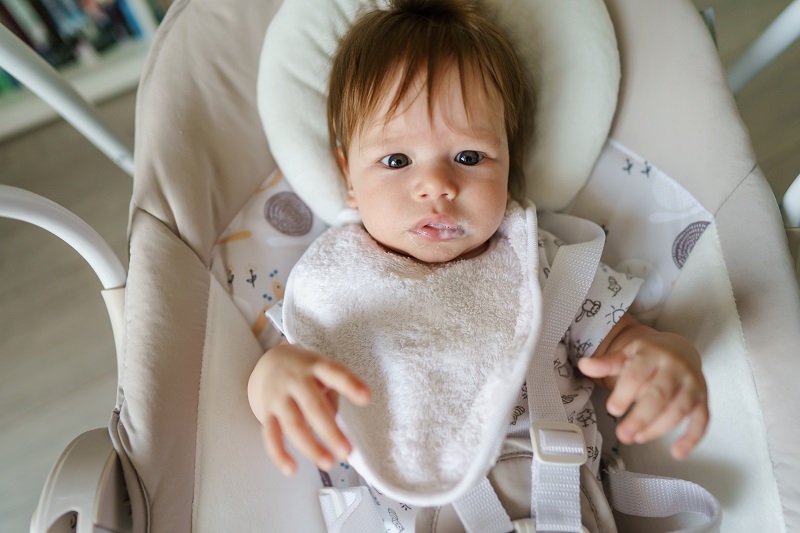 Baby with a bib spitting up after a bottle of milk