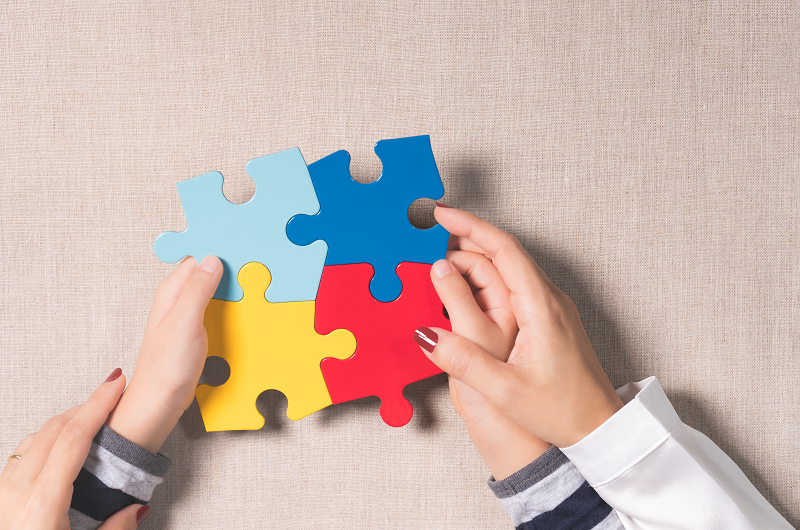, Close-up, Top view of mother's hands holding autistic young child's hands holding colorful jigsaw puzzles (yellow, red, blue, light blue) on beige linen cloth. World autism awareness day support concept.