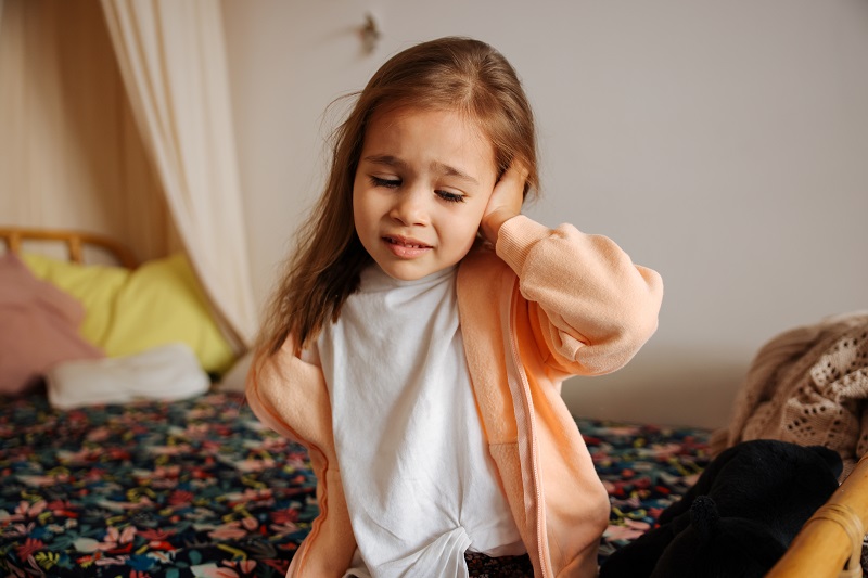 Young girl holding her ear in pain from a potential ear infection