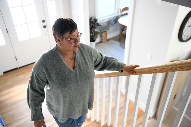 Woman walking up the stairs holding on to the railing.