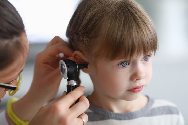 Otorhinolaryngologist examines a little girl's ear with an otoscope.