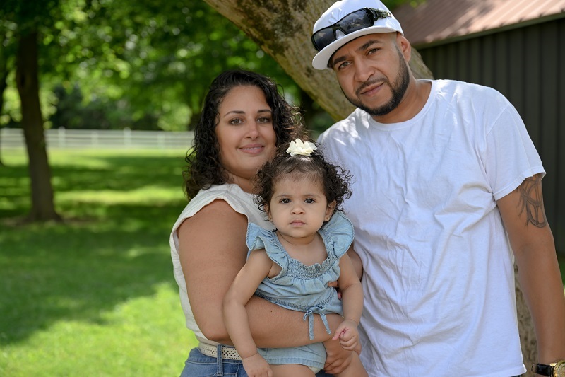 A mother, father and daughter, the Lopez family, smiling in the park.