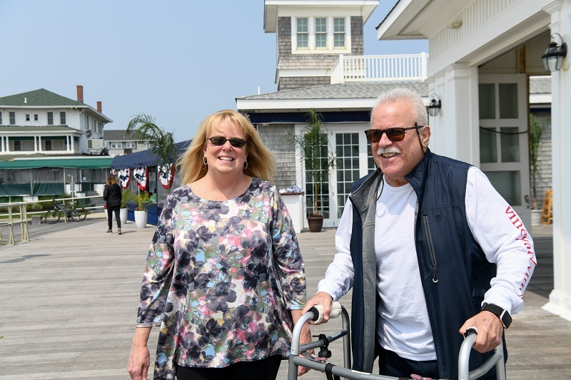 Tom and his wife walking on the boardwalk smiling.