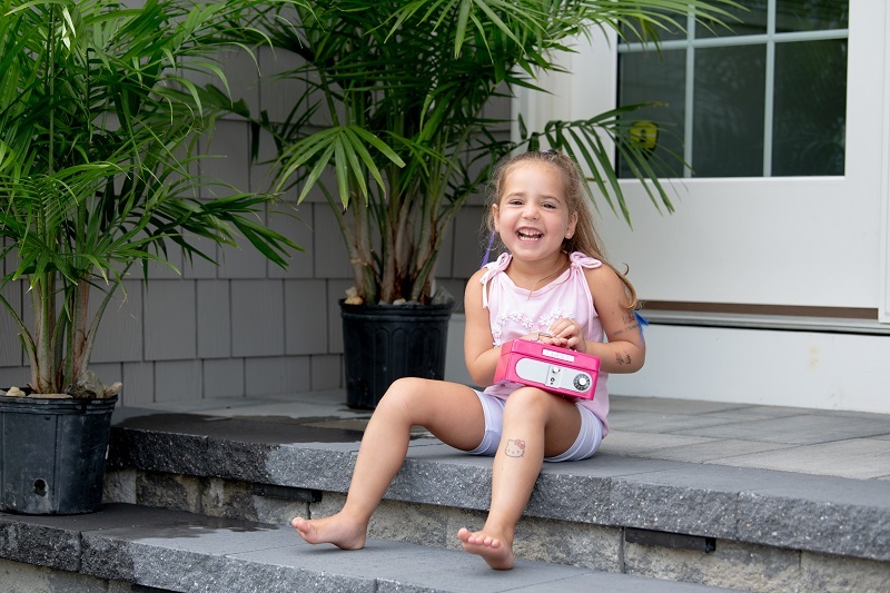 Toddler Maddie Troeller smiling on the front step with her piggy bank.