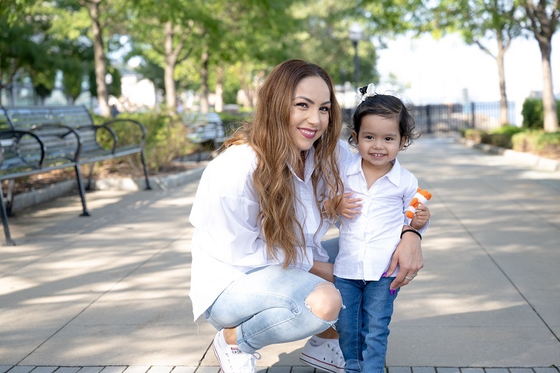 Marisol and her young daughter standing in the park smiling together.