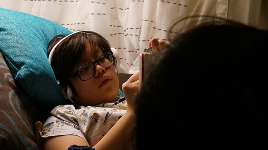 A young Jasmine S, laying in bed with headphones on, sketching on a pad. 