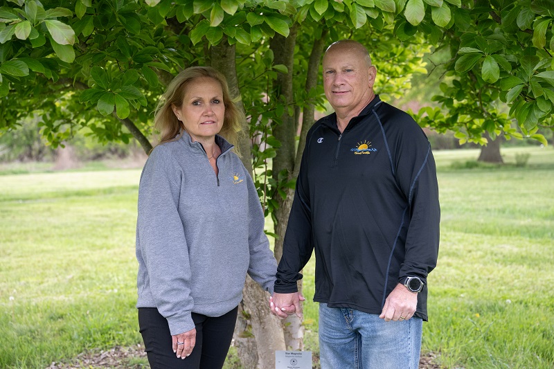 Stu and Michele Schulman standing outside, holding hands, under a tree.
